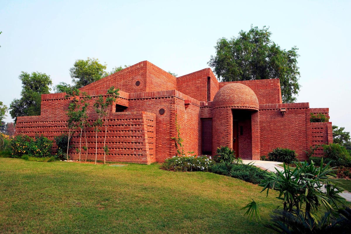 A large brick building with a dome and multiple windows, surrounded by a well-maintained lawn and trees.
