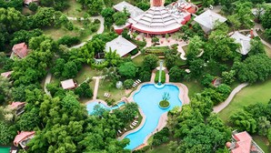 An aerial view of a resort with a central swimming pool, surrounded by lush greenery and multiple buildings with red roofs. - The Westin Sohna Resort & Spa (Sohna)