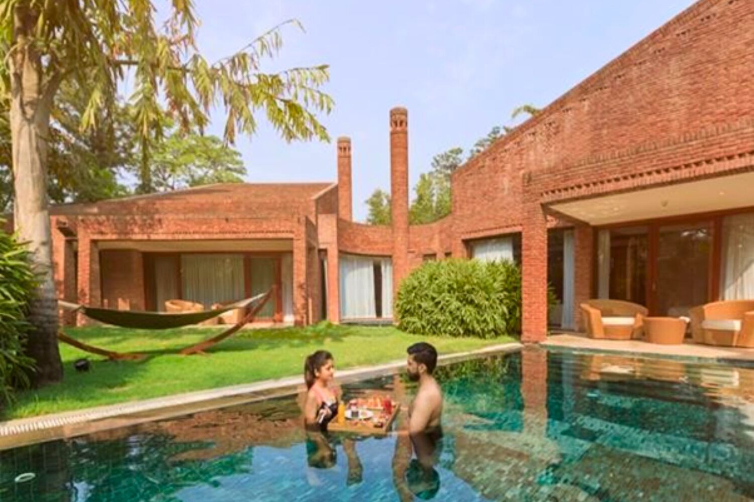 Une piscine avec un bâtiment en briques en arrière-plan, un hamac et un couple près de la piscine.