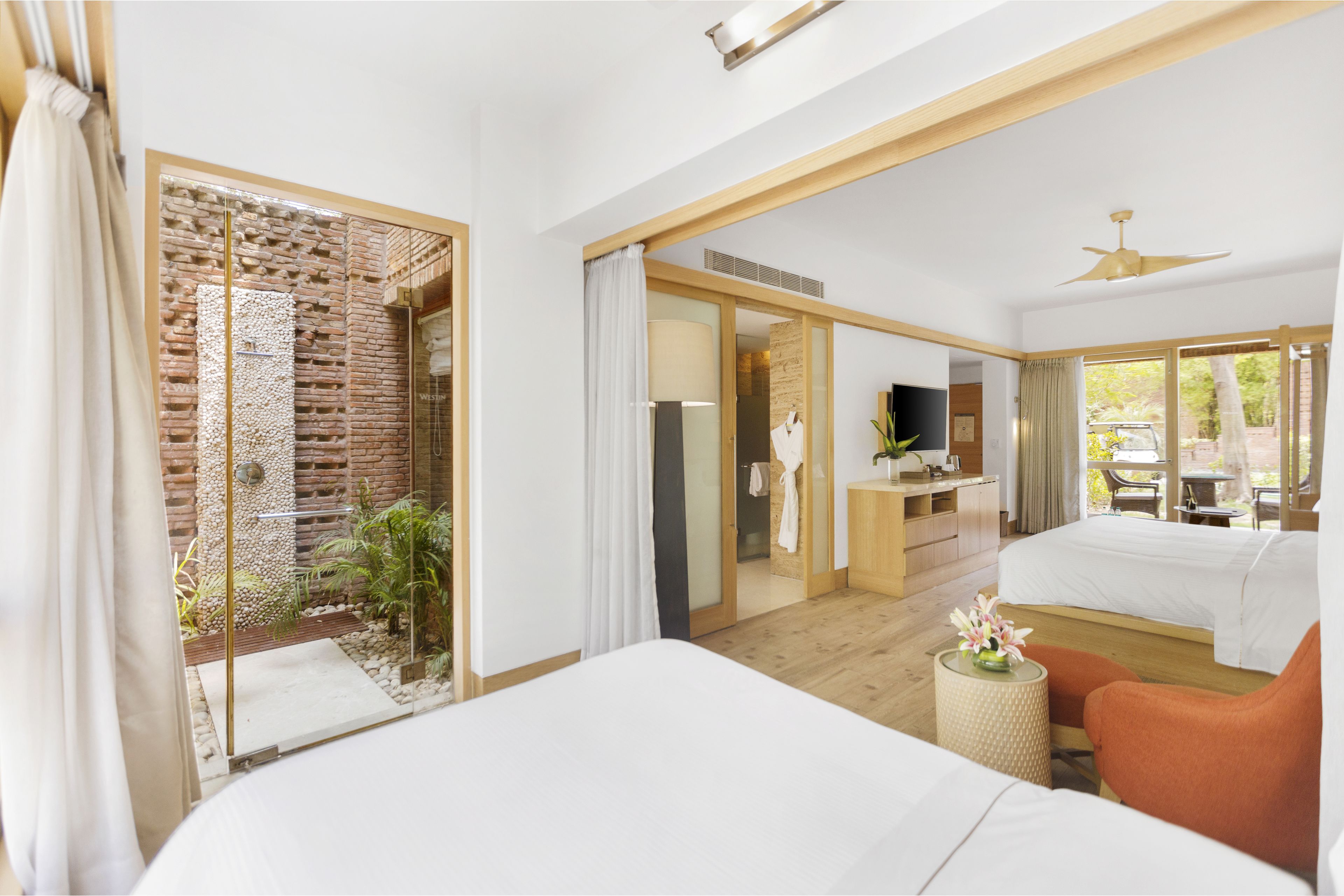 Quarto de hotel com cama grande, escrivaninha com televisão, um cantinho para sentar e vista para o exterior.