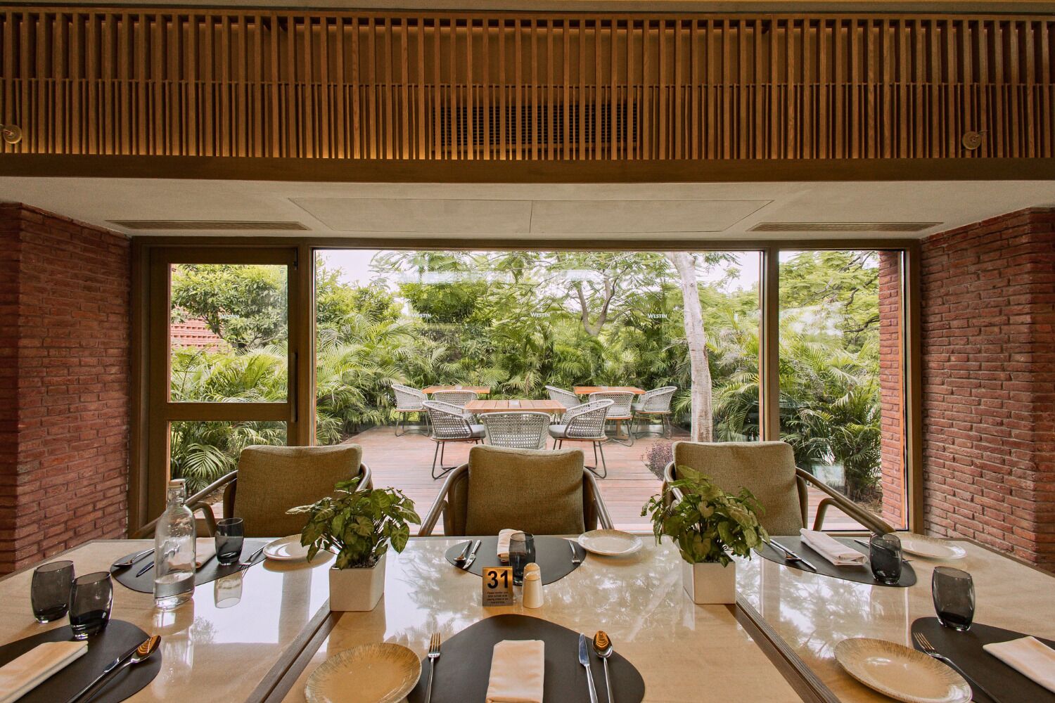 A dining area with a large table, chairs, and a view of a lush garden through large windows.