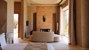 Un espacioso dormitorio con una cama grande, una zona de estar curvada, una chimenea y vistas al exterior.