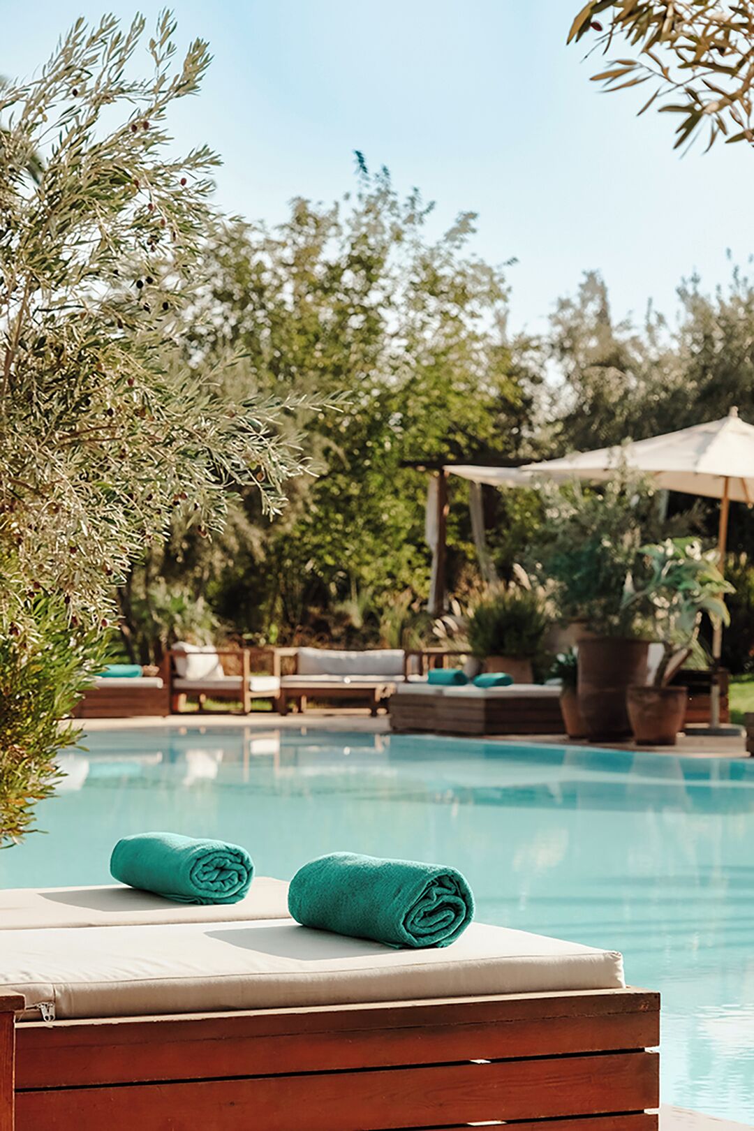 Un área junto a la piscina con terraza de madera, sillas de descanso y una pérgola.