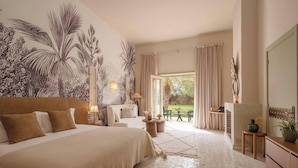Un dormitorio amplio con una cama grande, una zona de estar, vistas al jardín y una pared decorada con motivos de plantas tropicales.
