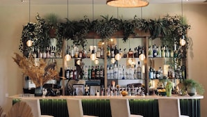 Zona de bar con lámparas de mimbre colgantes, mostrador de bar verde y estantes llenos de botellas de licores.