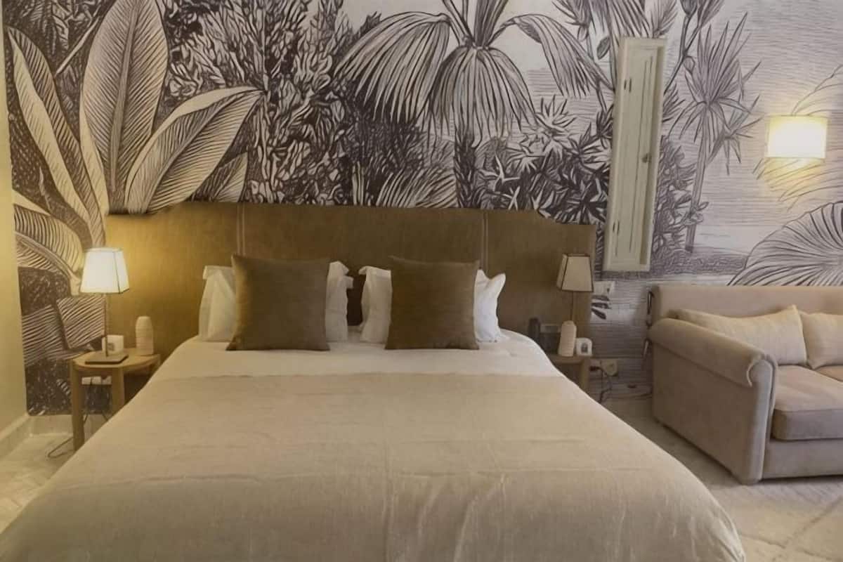 A bedroom with a large bed, a headboard, bedside tables with lamps, and a couch.