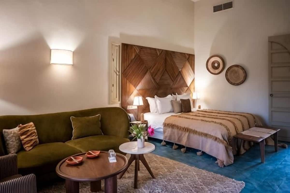 A hotel room with a bed, a sofa, a small table, and a decorative wall panel.