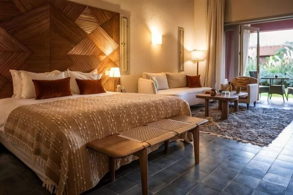 A hotel room with a large bed, a sofa, a small table, and a bench.