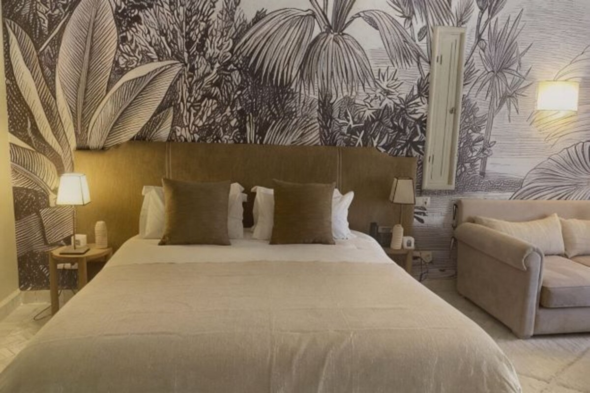 A bedroom with a large bed, a headboard, bedside tables with lamps, and a couch.
