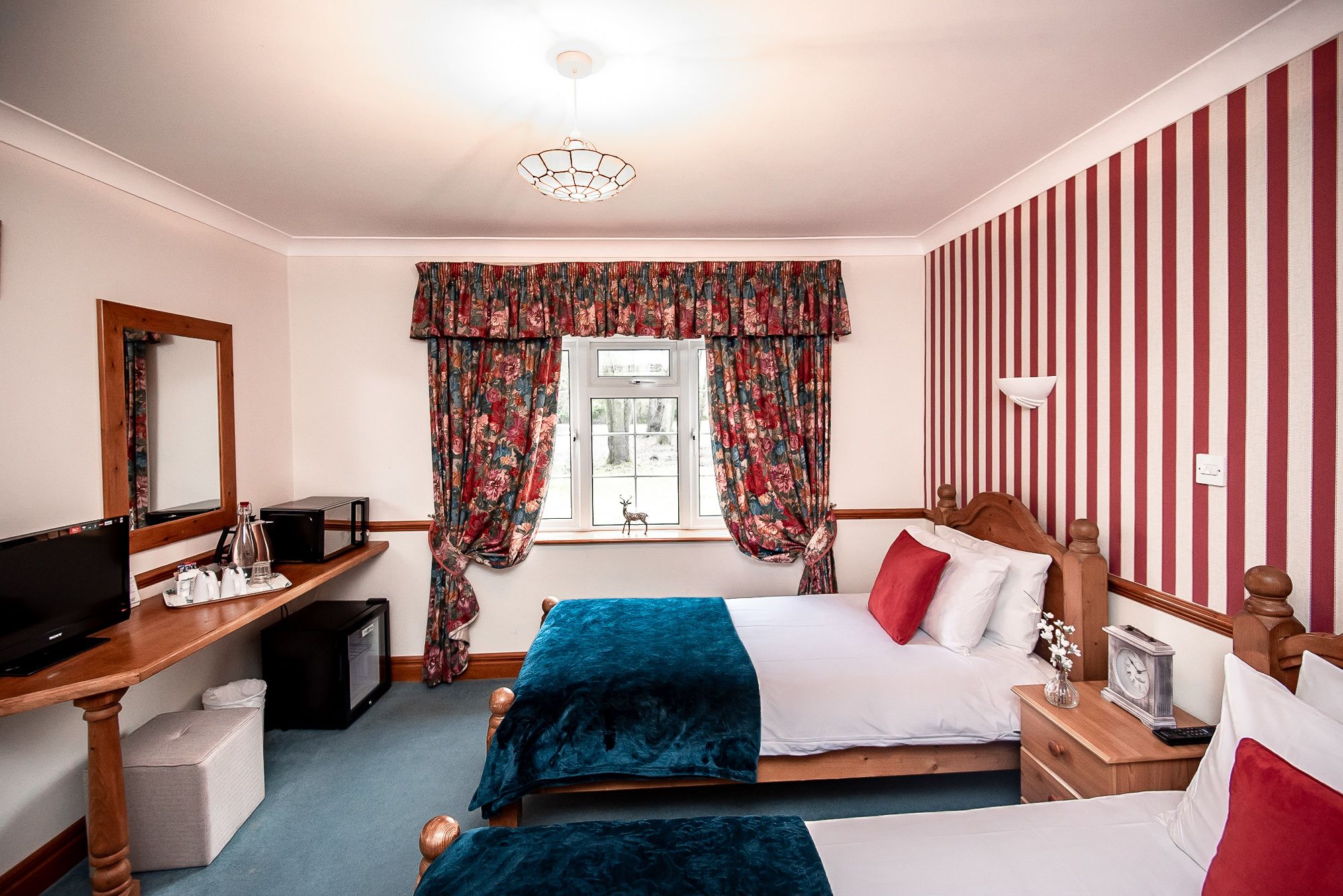 Een hotelkamer met een bed, een bureau met een computer, een televisie en een raam met gordijnen.