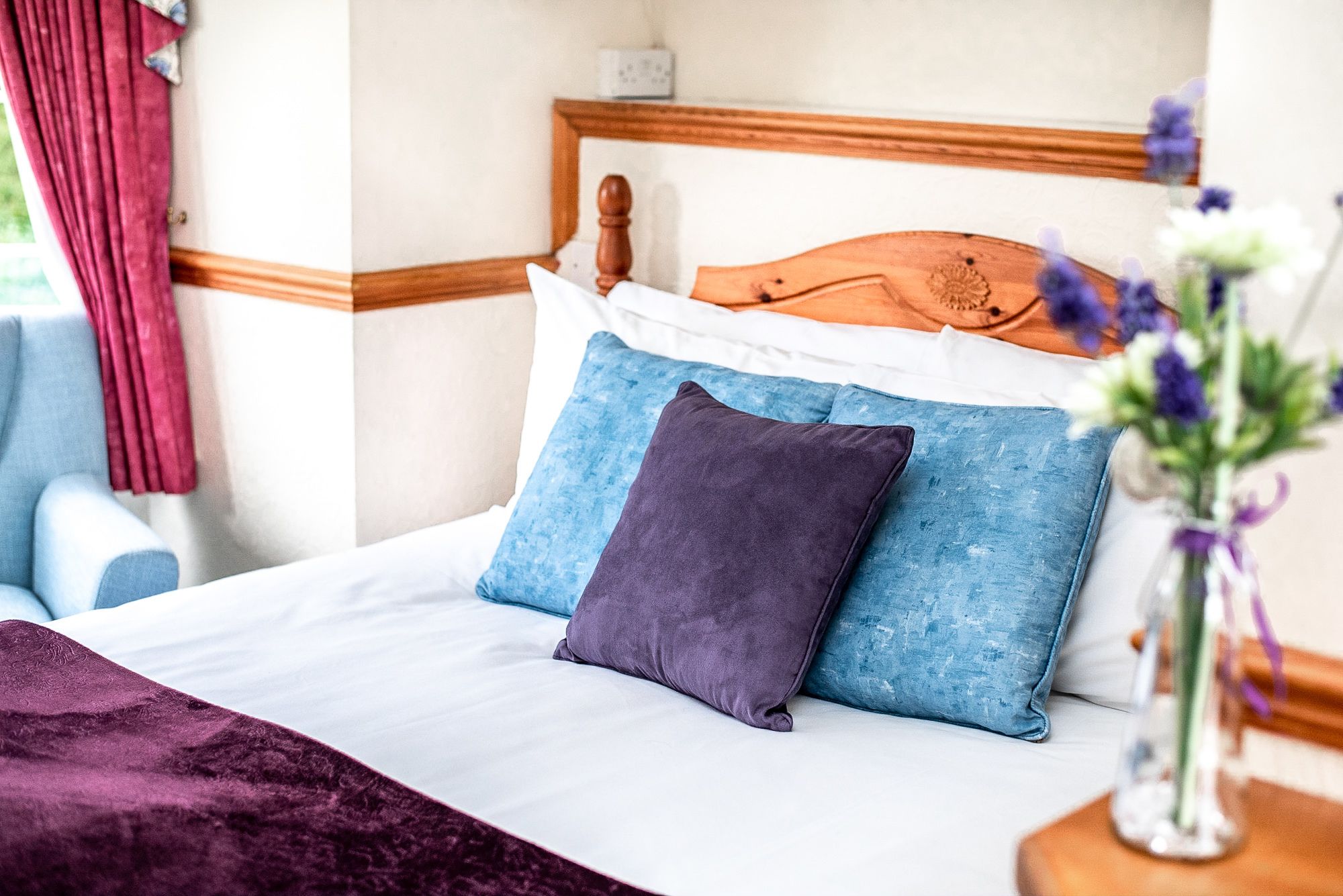 A neatly made bed with a wooden headboard, two pillows, and a purple throw blanket.