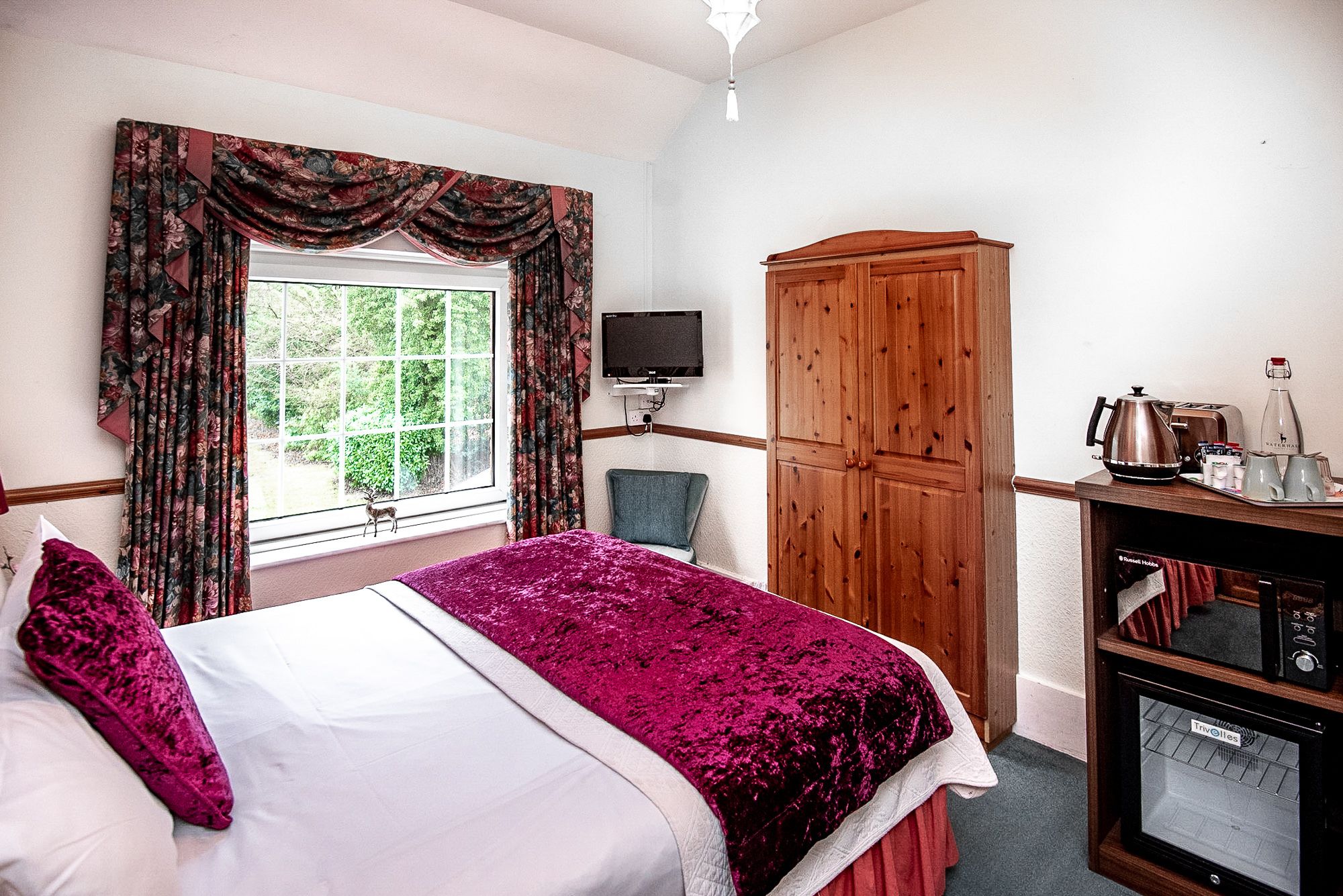 A hotel room with a bed, a television, a wardrobe, and a kitchenette.