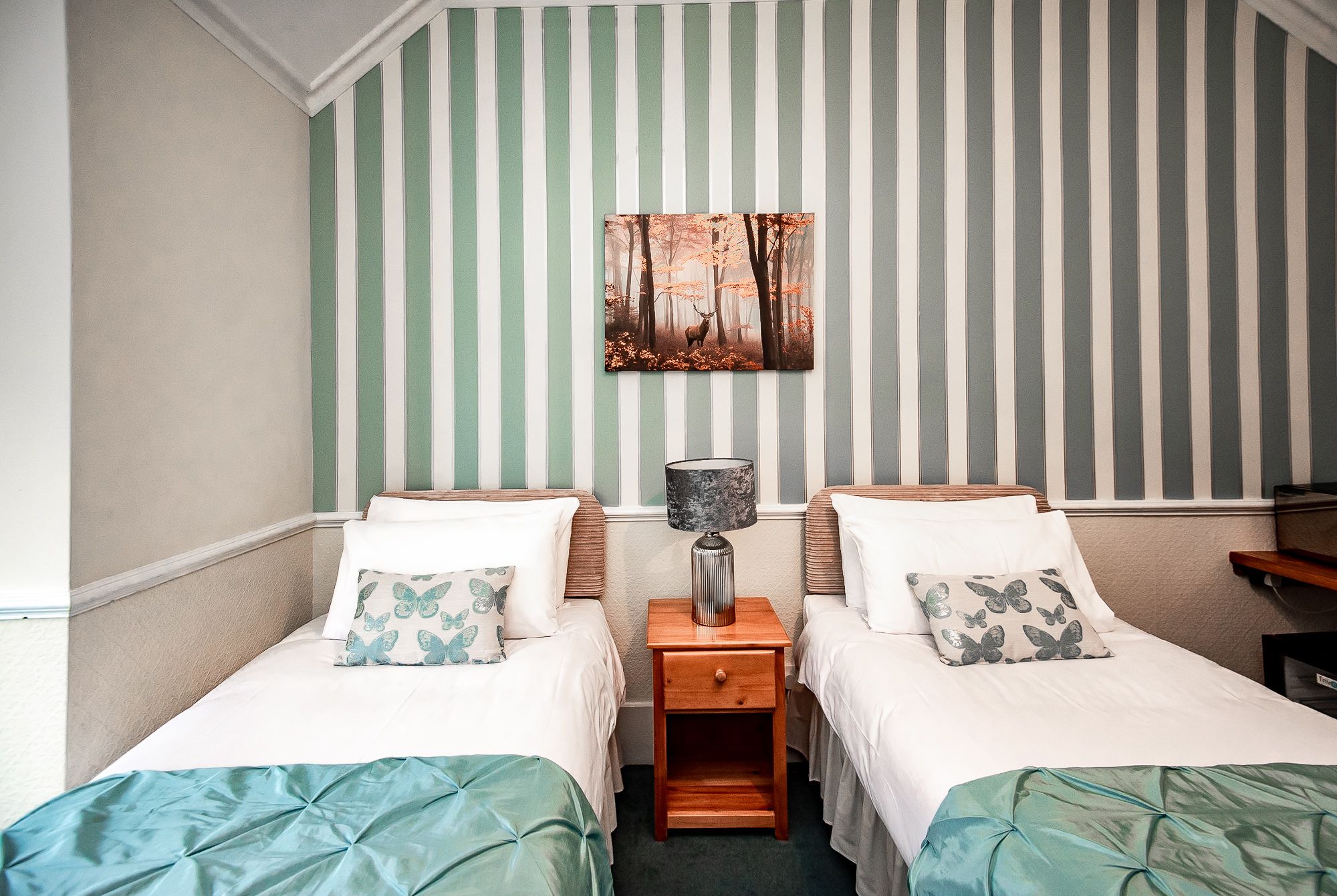A room with two single beds, a nightstand with a lamp, and a framed picture on the wall.