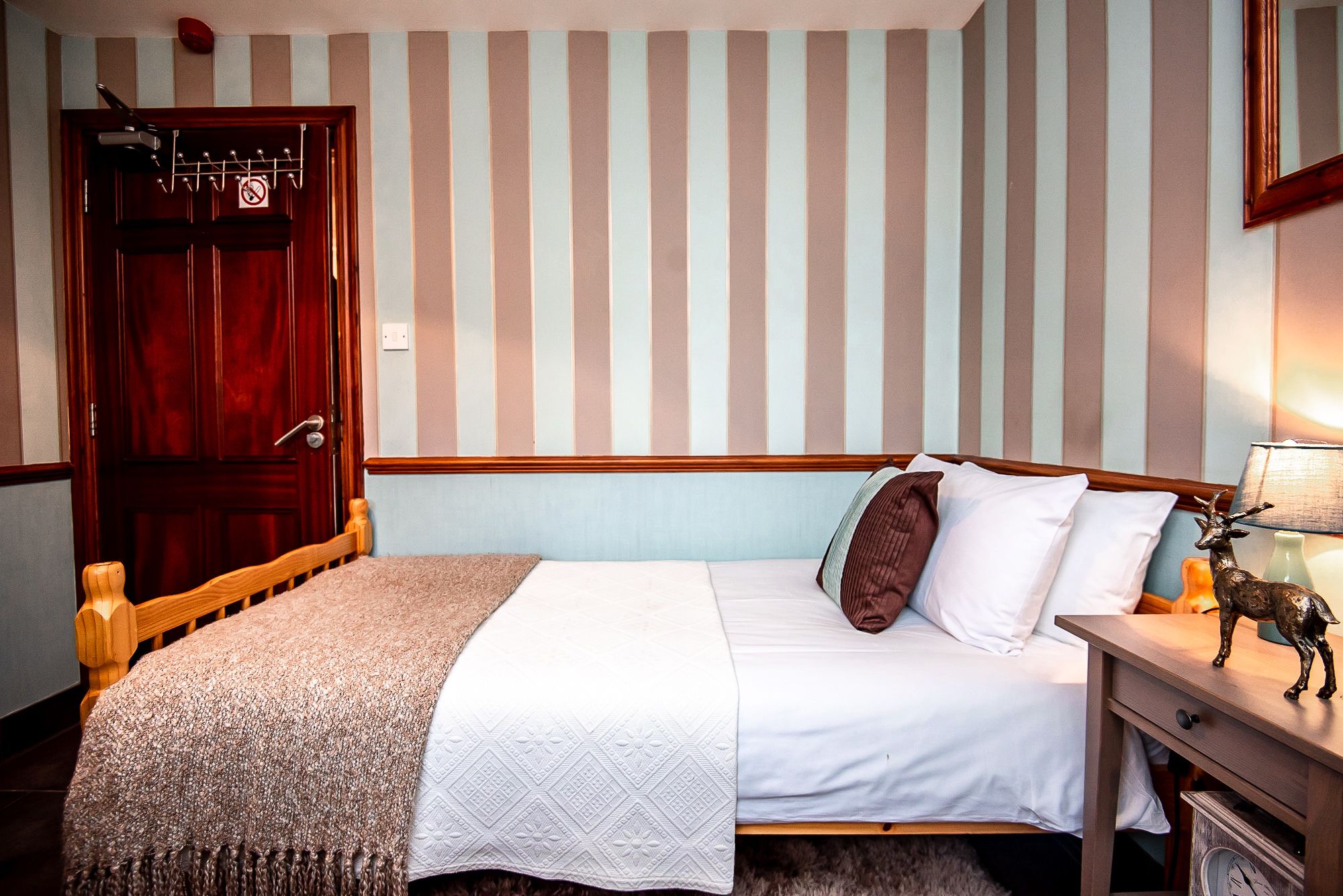 A bedroom with a wooden bed, a nightstand, a lamp, and a door with a coat rack.