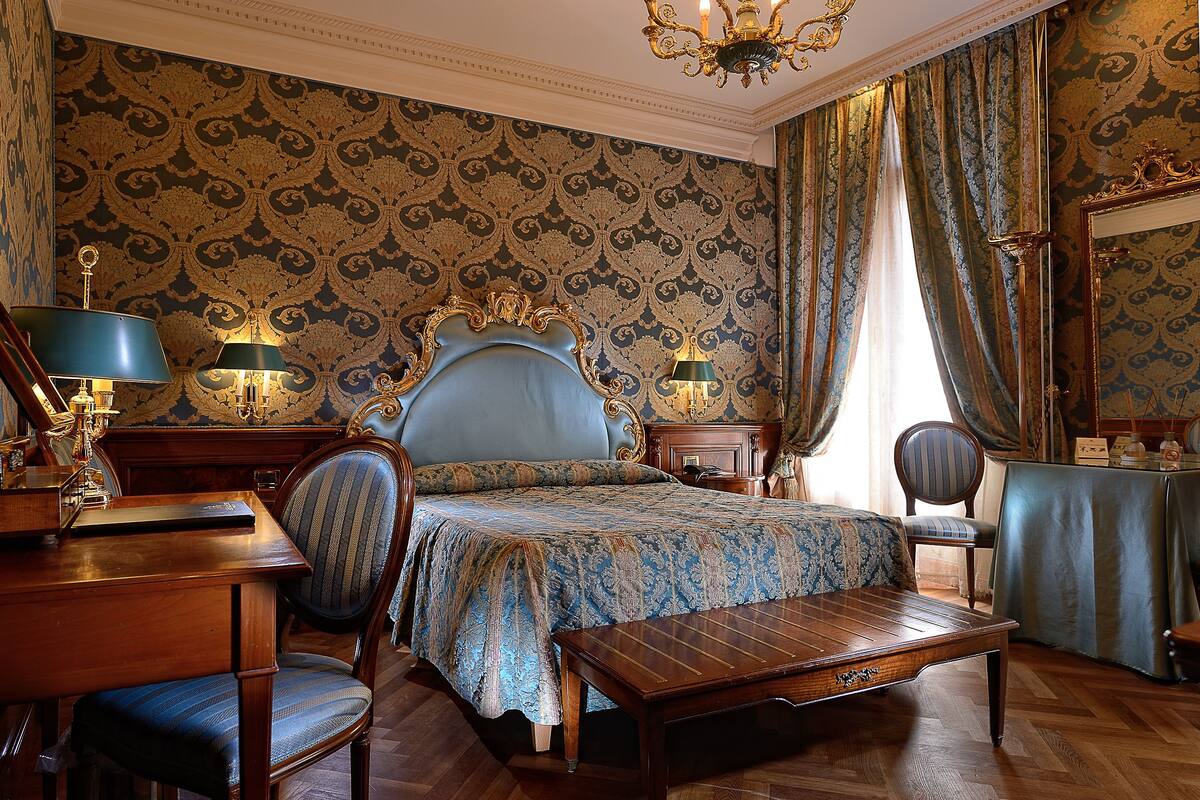 A classic, elegantly furnished bedroom with a large bed, a wooden desk, and a chair.