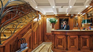 A grand lobby with a marble staircase, a reception desk, and a large mirror.