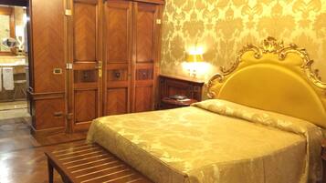 Une chambre d’hôtel avec un lit, un banc en bois, une armoire et une table de chevet avec une lampe.