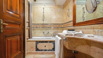 A luxurious bathroom with marble flooring, a bathtub, a large mirror, and wooden cabinetry.
