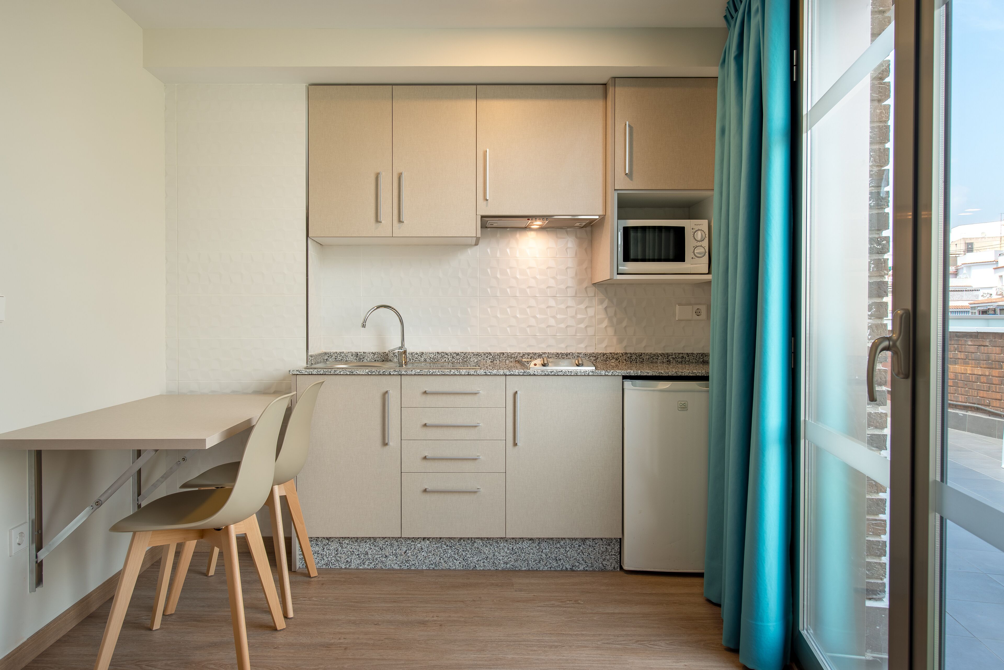 A modern kitchen with a dining area, a microwave, and a view through a window with curtains.