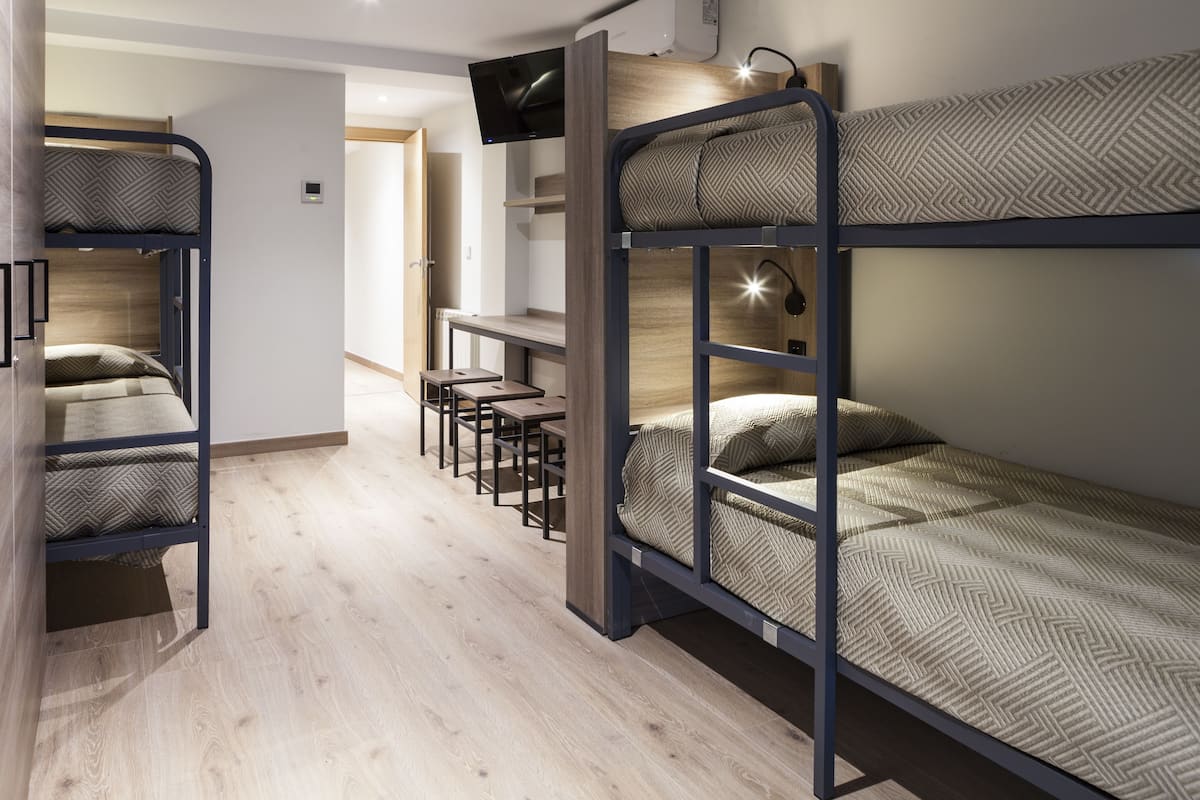 A modern, compact room with bunk beds, a desk, and a TV.