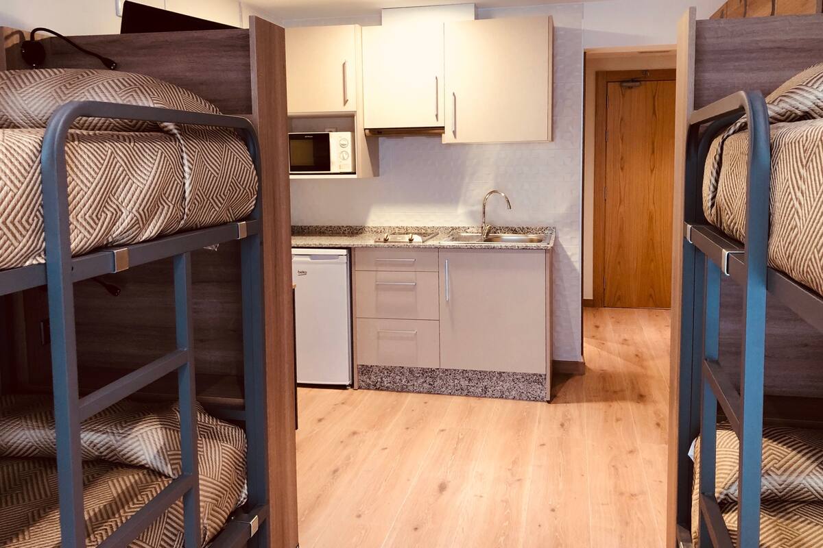 A compact room with bunk beds, a kitchenette, and a small bathroom.