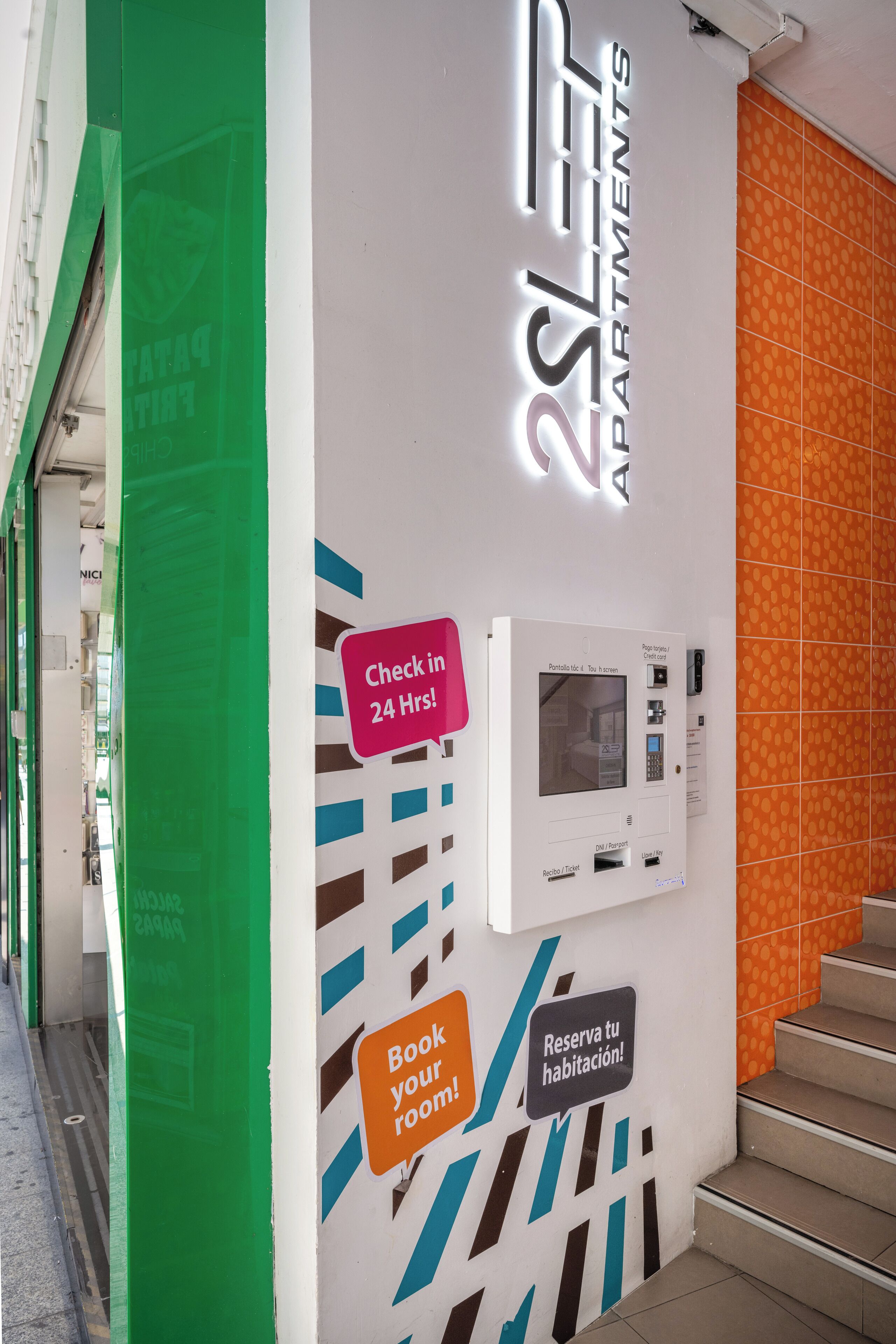 A wall with a check-in kiosk, a sign for 24-hour check-in, and a sign encouraging to book a room.