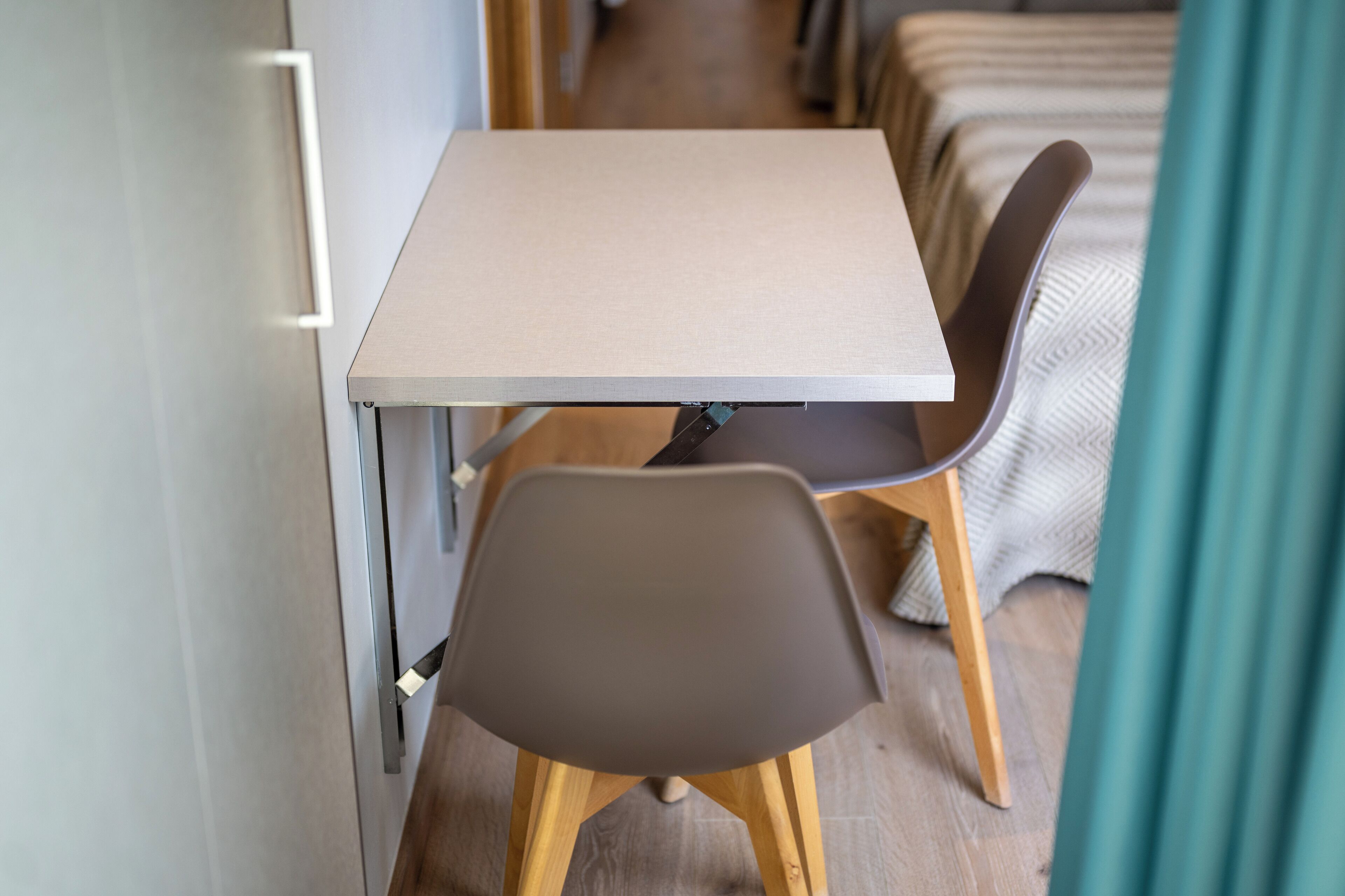Une pièce de taille modeste, avec une petite table et deux chaises, un lit recouvert d’une couverture à rayures et un plancher en bois.