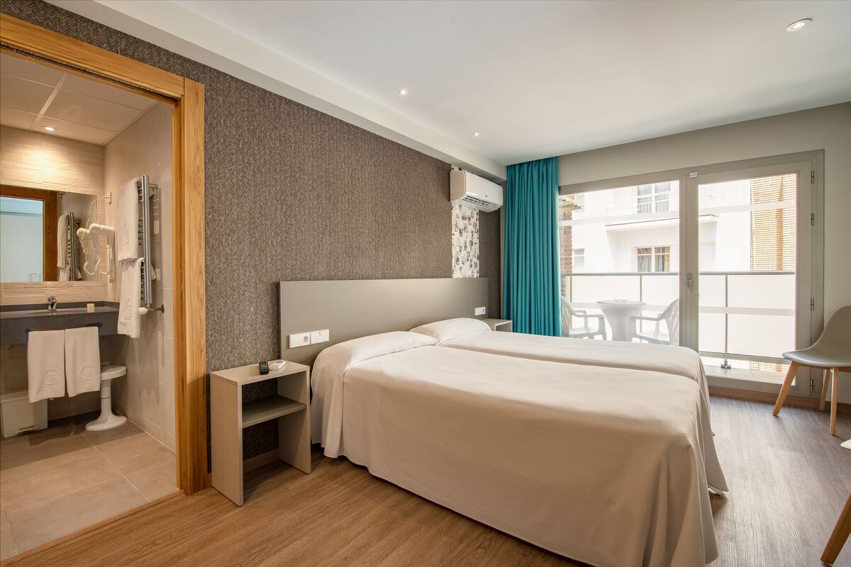 A modern hotel room with a large bed, a small desk, a mirror, and a bathroom with a toilet and sink.
