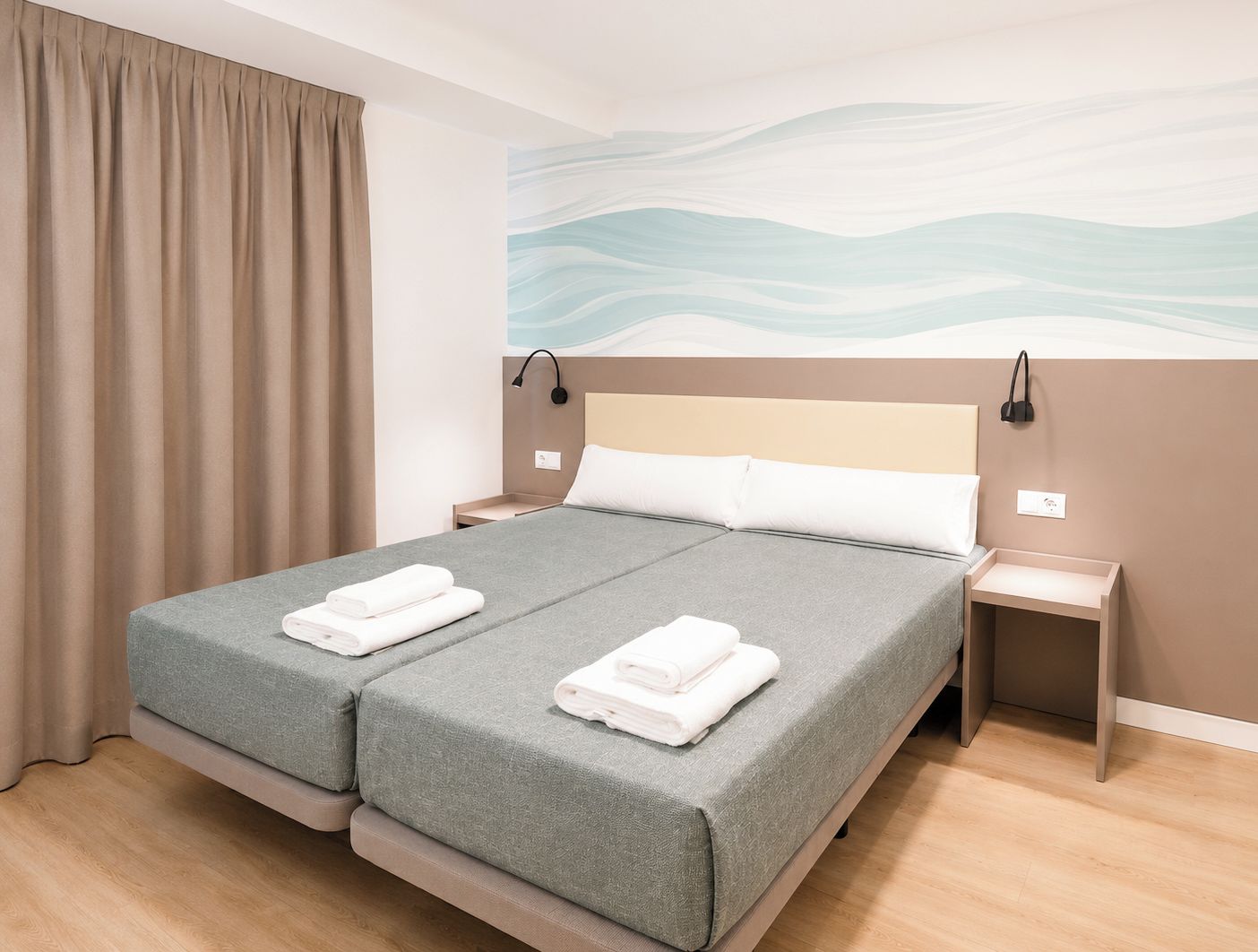 A double bed with grey bedding, two bedside tables, and a wall with a wave pattern.