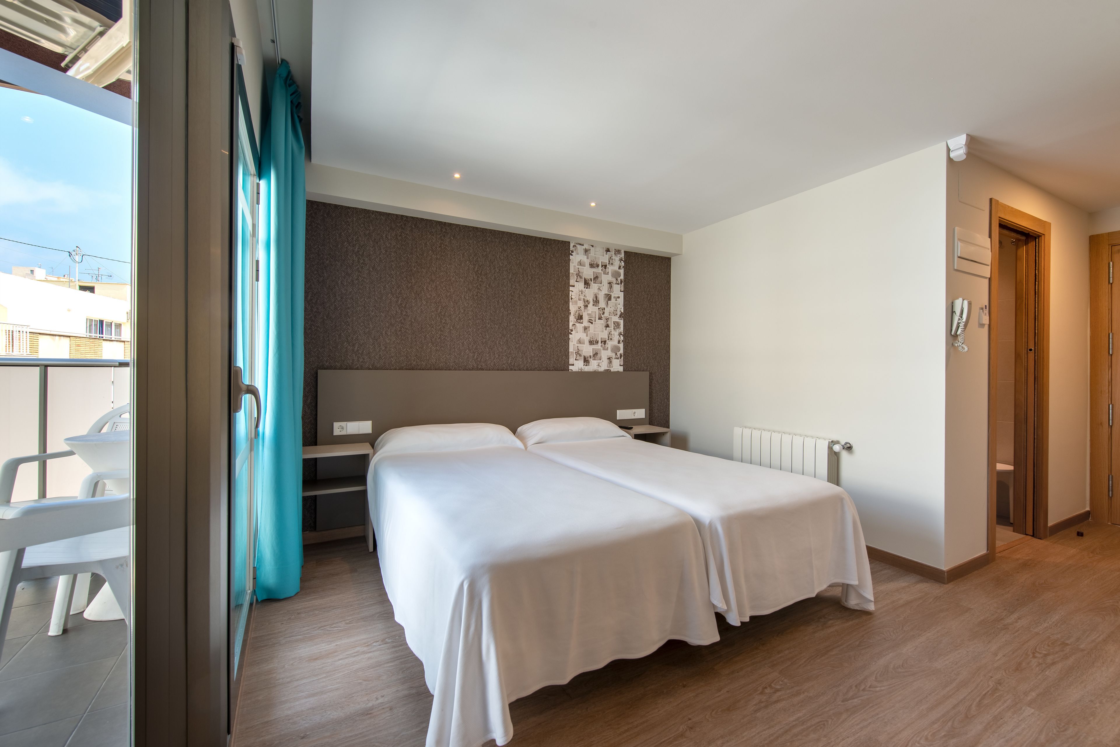 A hotel room with two beds, a view of the city, and a balcony with chairs.