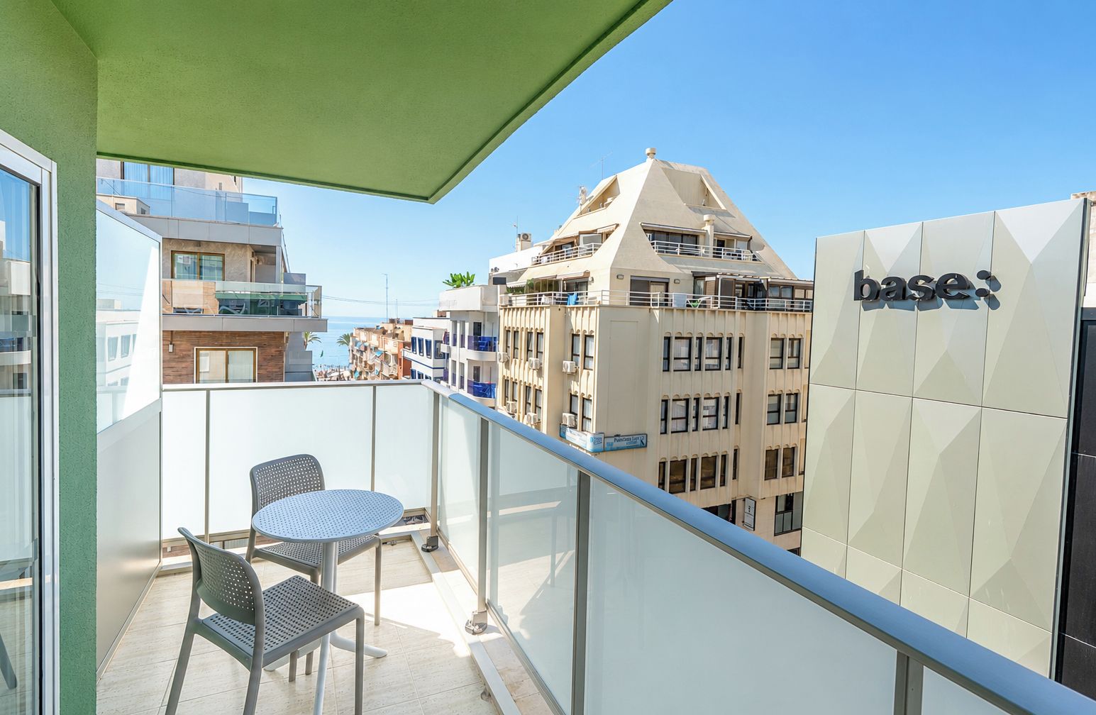 A balcony with a table and chairs, overlooking a cityscape with buildings and a clear sky.