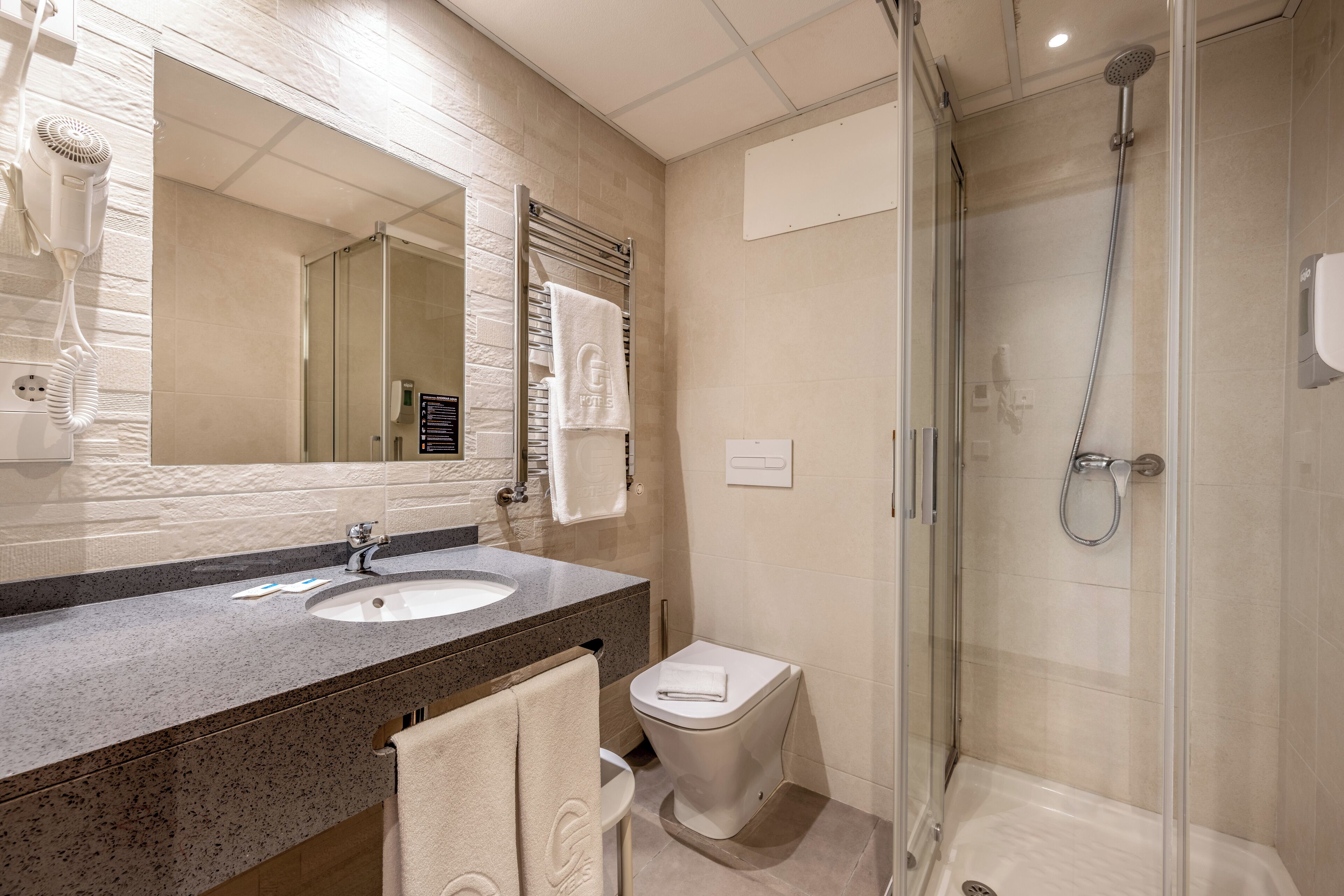 A modern bathroom with a granite countertop, a large mirror, a glass-enclosed shower, and a toilet.