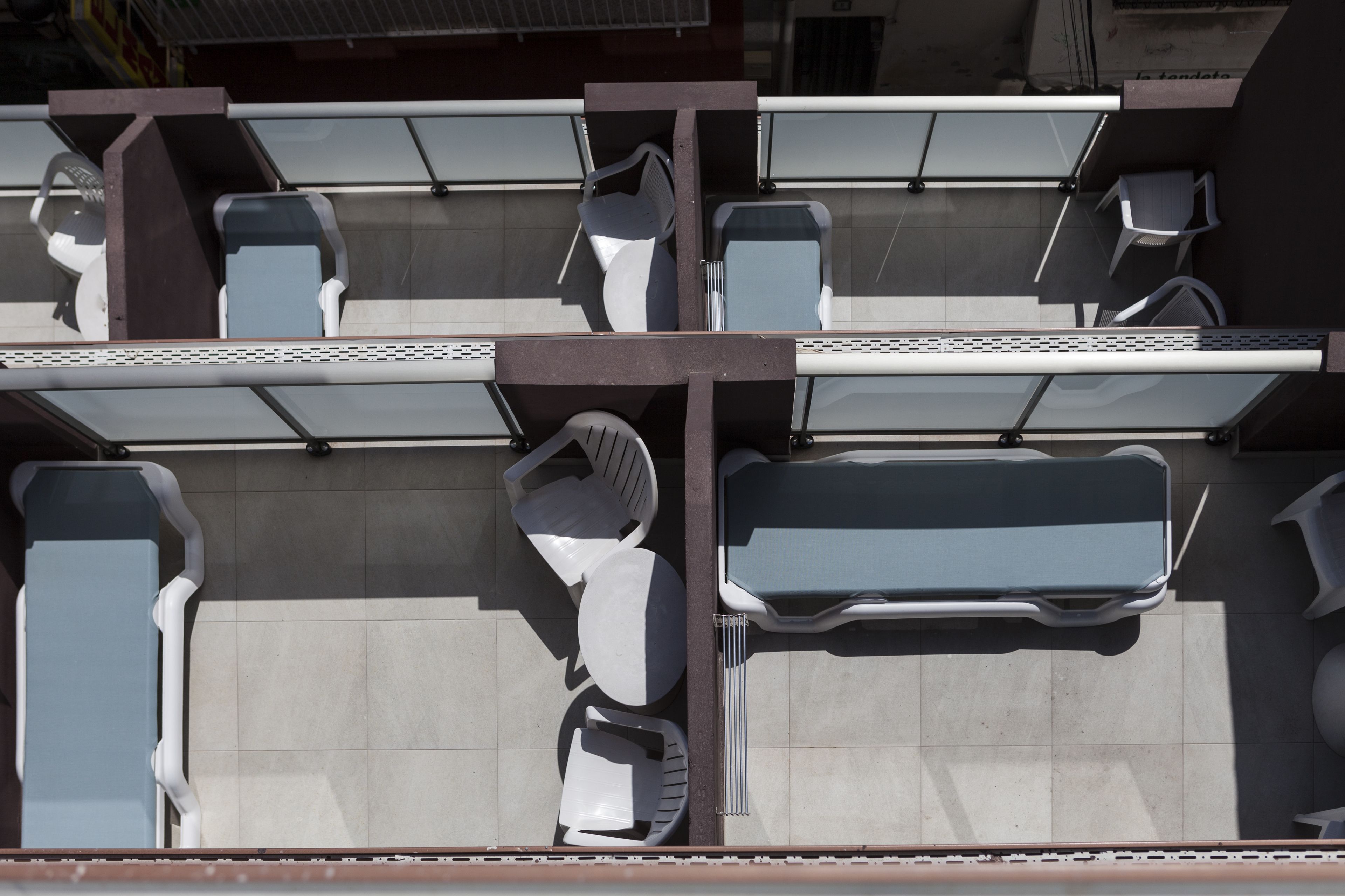 A top-down view of a hotel room with a balcony, featuring a seating area with chairs and a table, and a large window providing a view of the street.