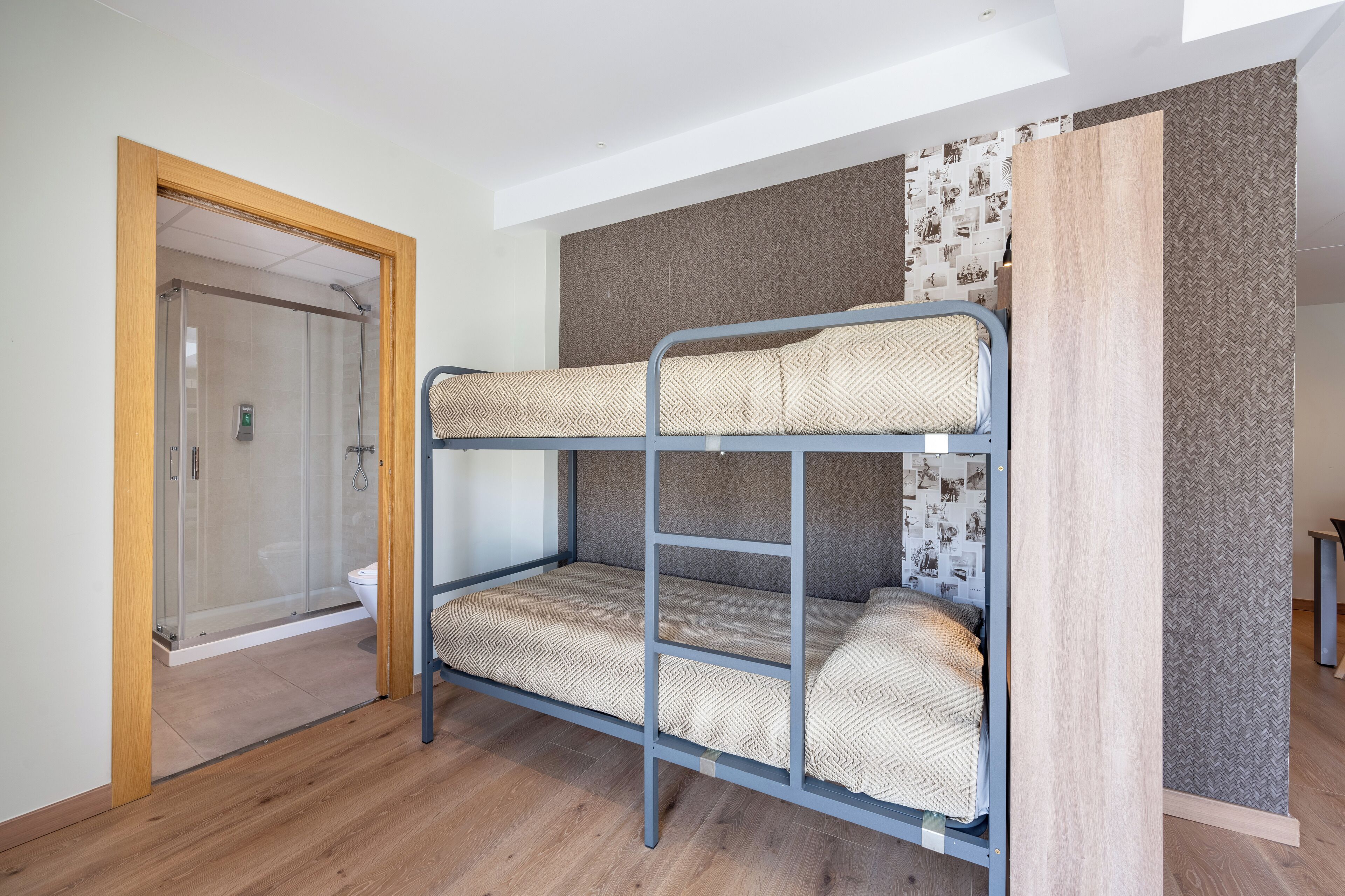 A bunk bed with patterned bedding in a room with wooden flooring and a shower area.