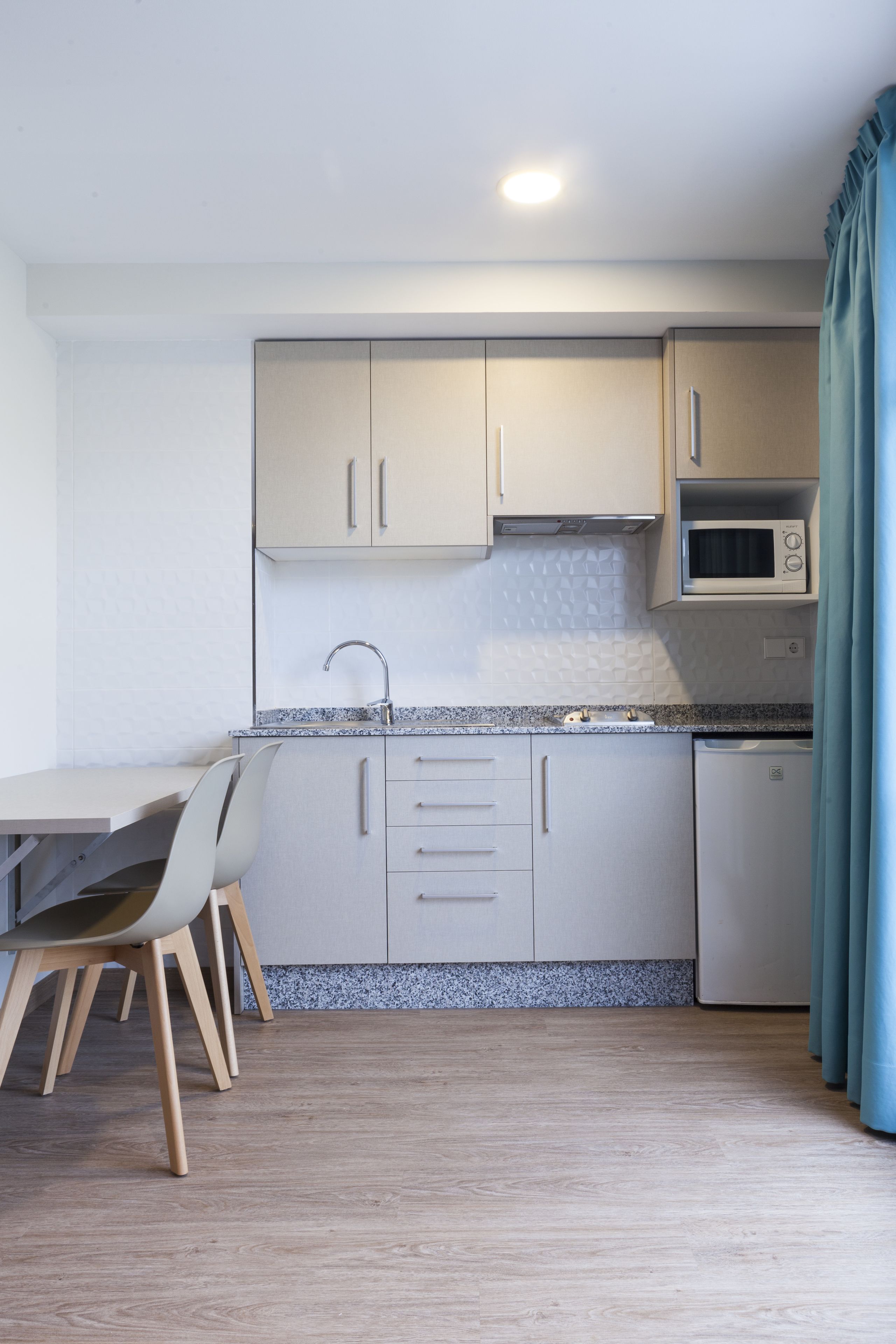 A compact kitchen with a dining area, featuring a microwave, sink, and cabinets.