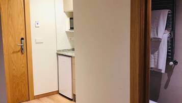 Een smalle gang met een houten deur, een kleine kitchenette en een toilet dat door een open deur zichtbaar is.