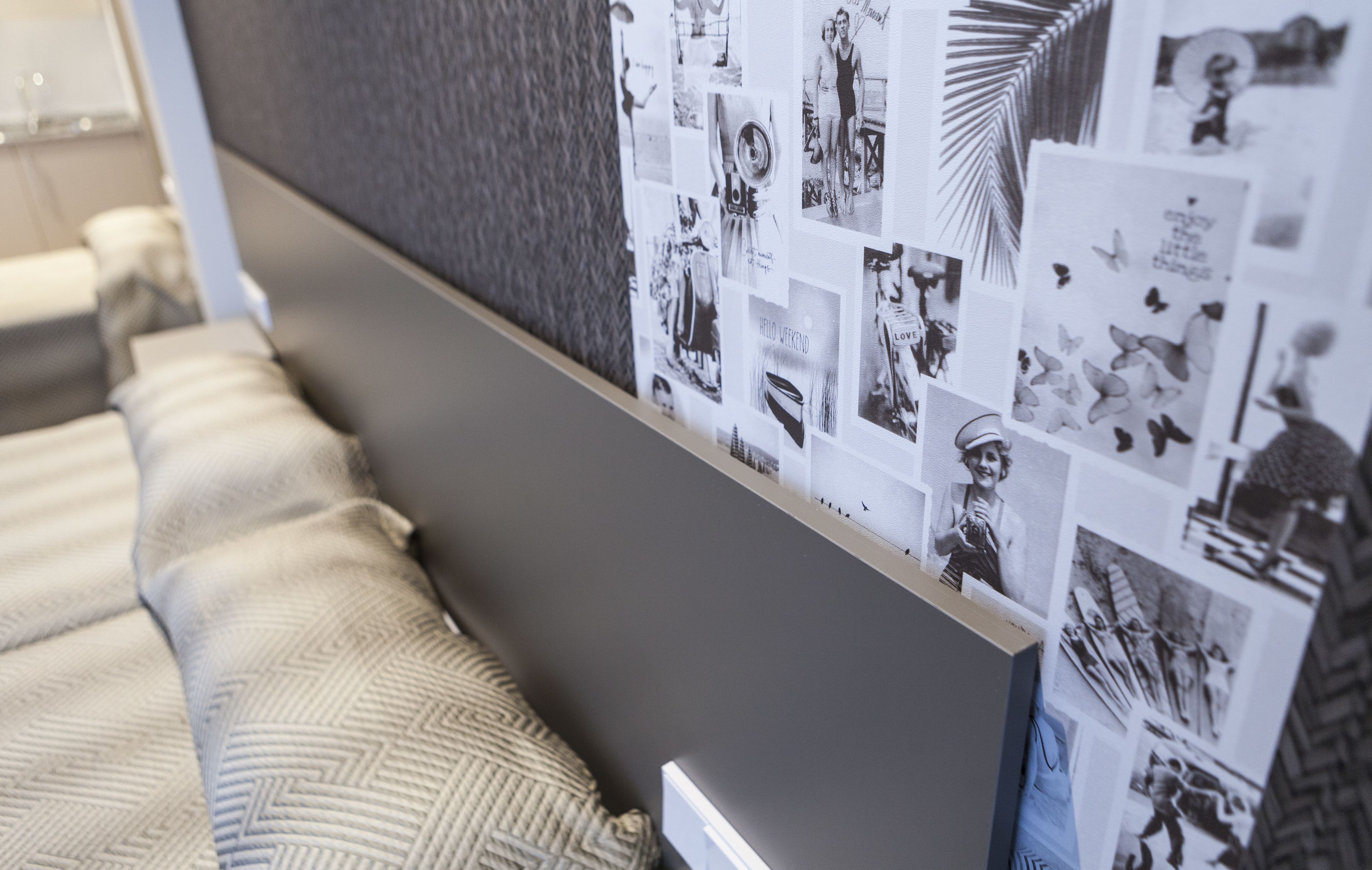 A wall with a collage of black and white photos, a patterned rug, and a bed with pillows.