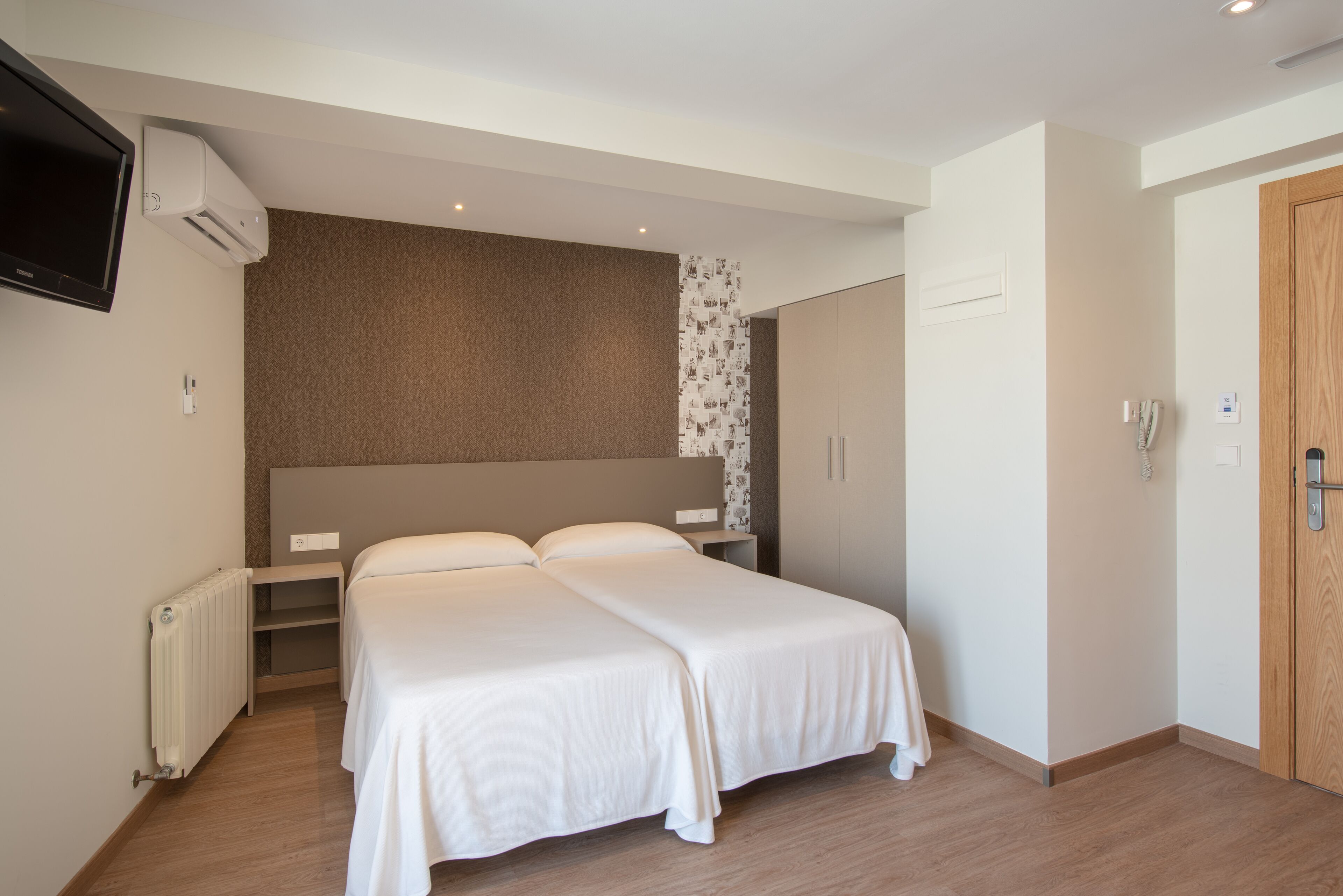 Habitación de hotel con cama doble, televisor montado en la pared, radiador y armario.