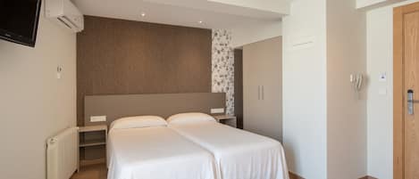 Habitación de hotel con cama doble, televisor montado en la pared, radiador y armario.