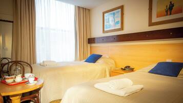 A hotel room with two beds, a dining table with tea set, and a painting on the wall.