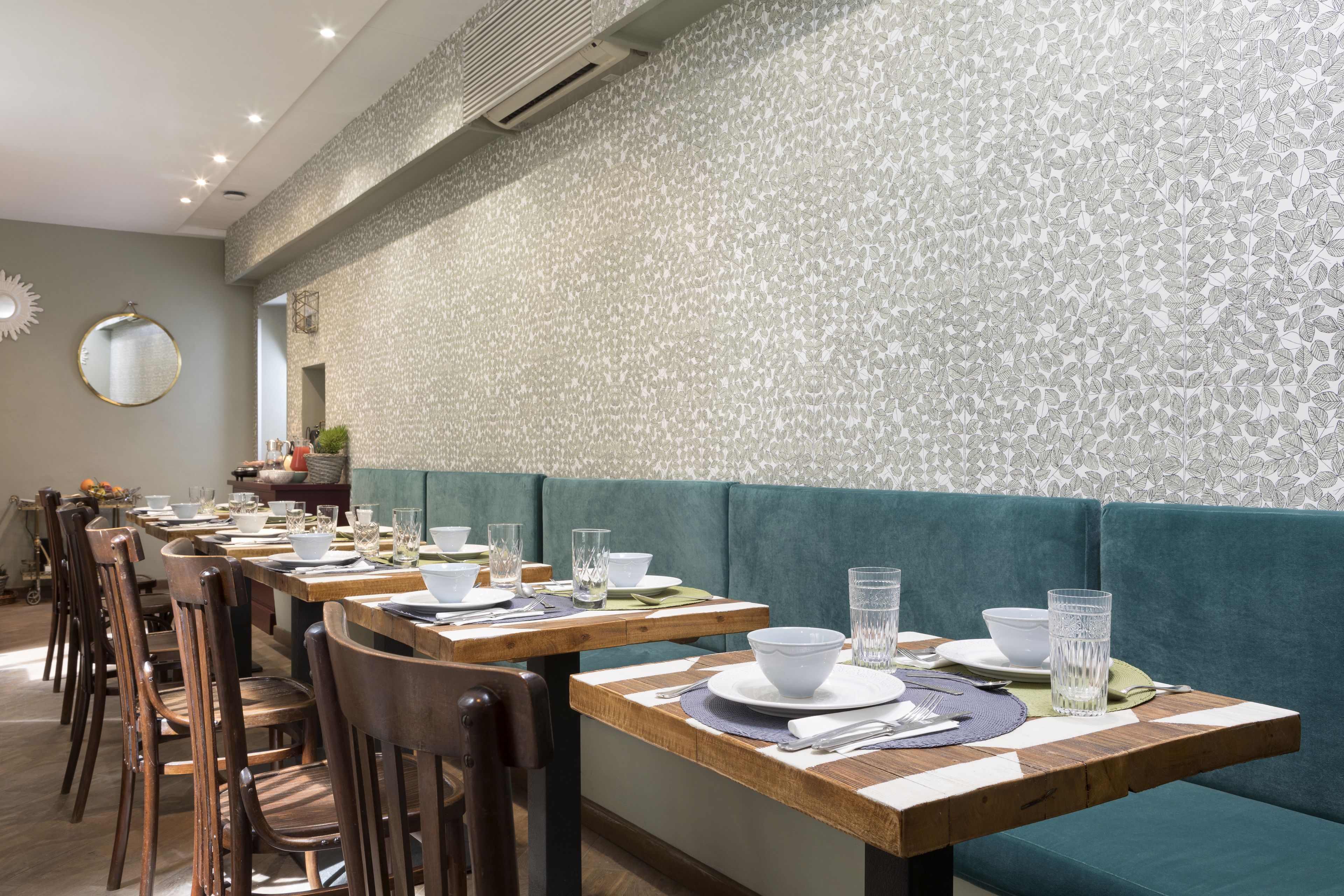 A restaurant with wooden tables and teal cushioned booths, equipped with white tableware and glassware.