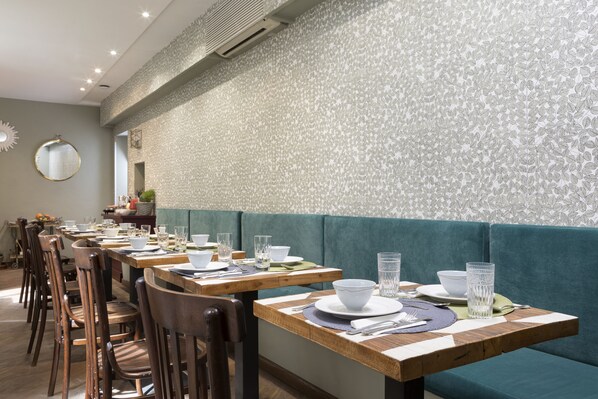 A restaurant with wooden tables and teal cushioned booths, equipped with white tableware and glassware.