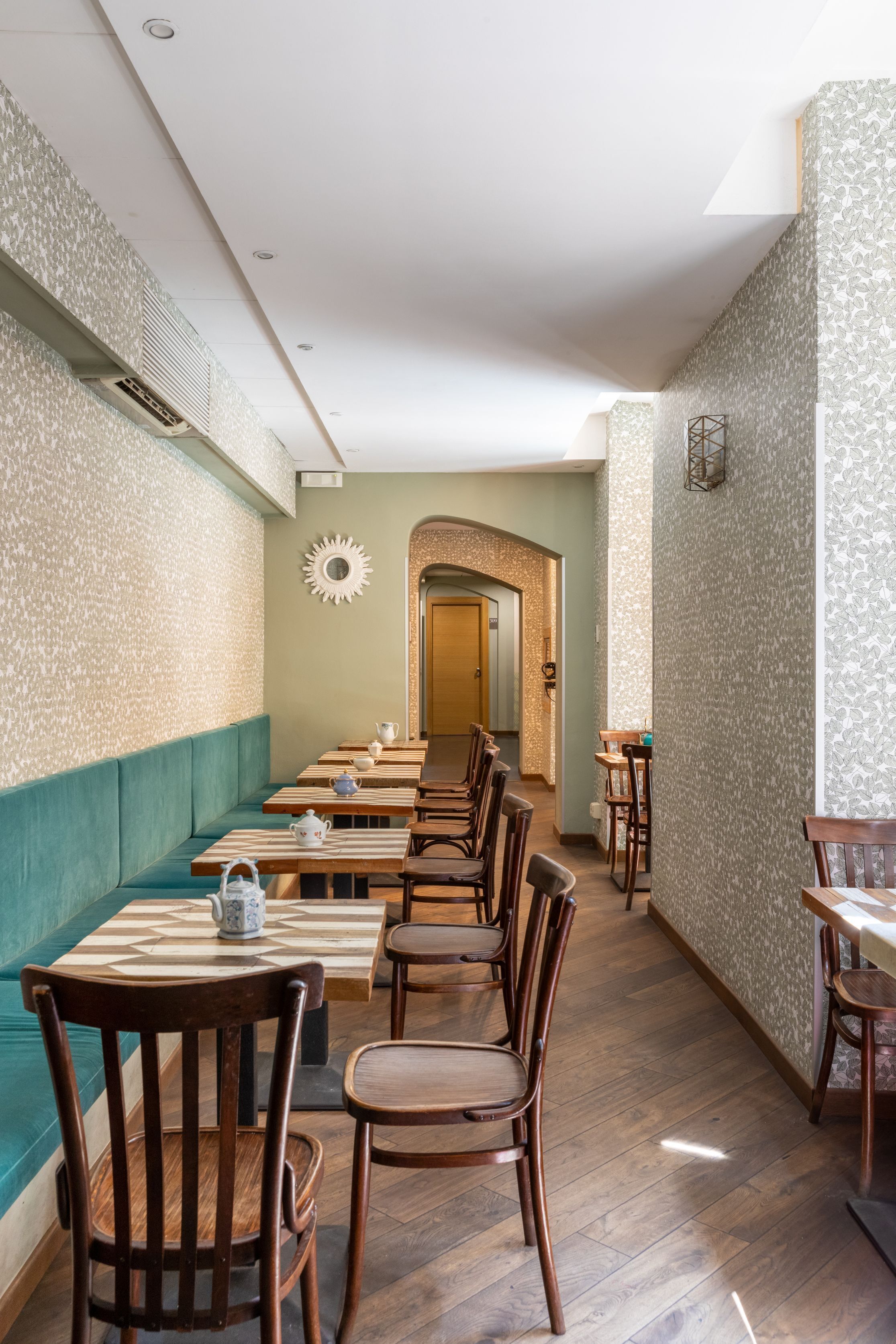 A restaurant interior with wooden tables and chairs, patterned wallpaper, and a sun-shaped wall decoration.