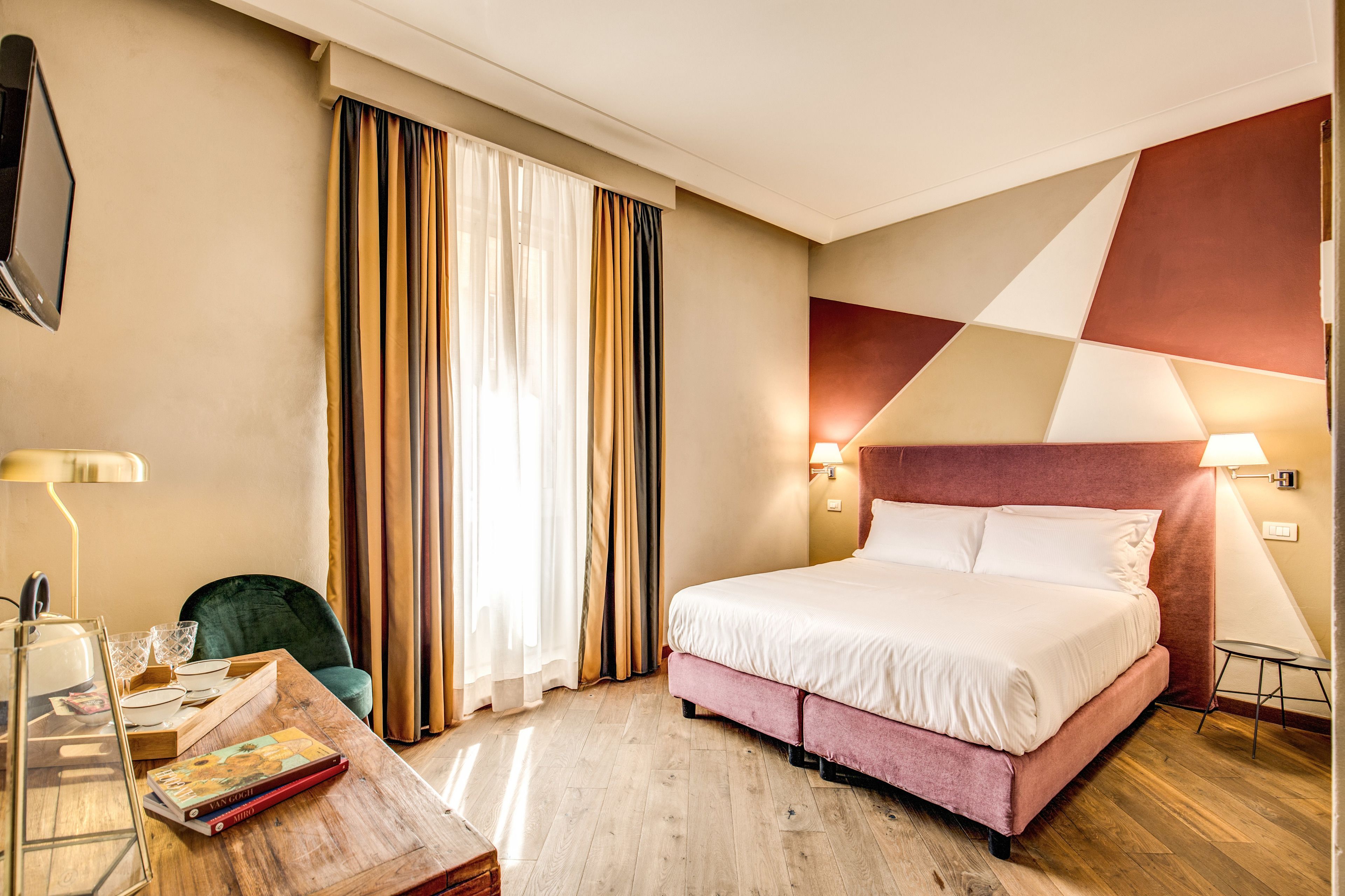 A hotel room with a bed, a desk, a chair, a TV, and a window with curtains.