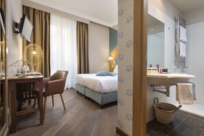 A hotel room with a bed, bedside table, lamp, chair, and a bathroom with a sink and mirror. - Boutique Hotel Galatea (Rome)