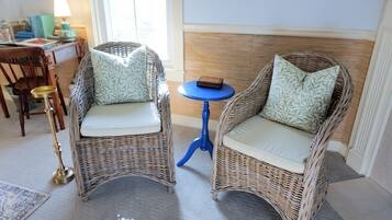 Deux fauteuils en osier avec des coussins, une petite table bleue et une lampe en laiton.