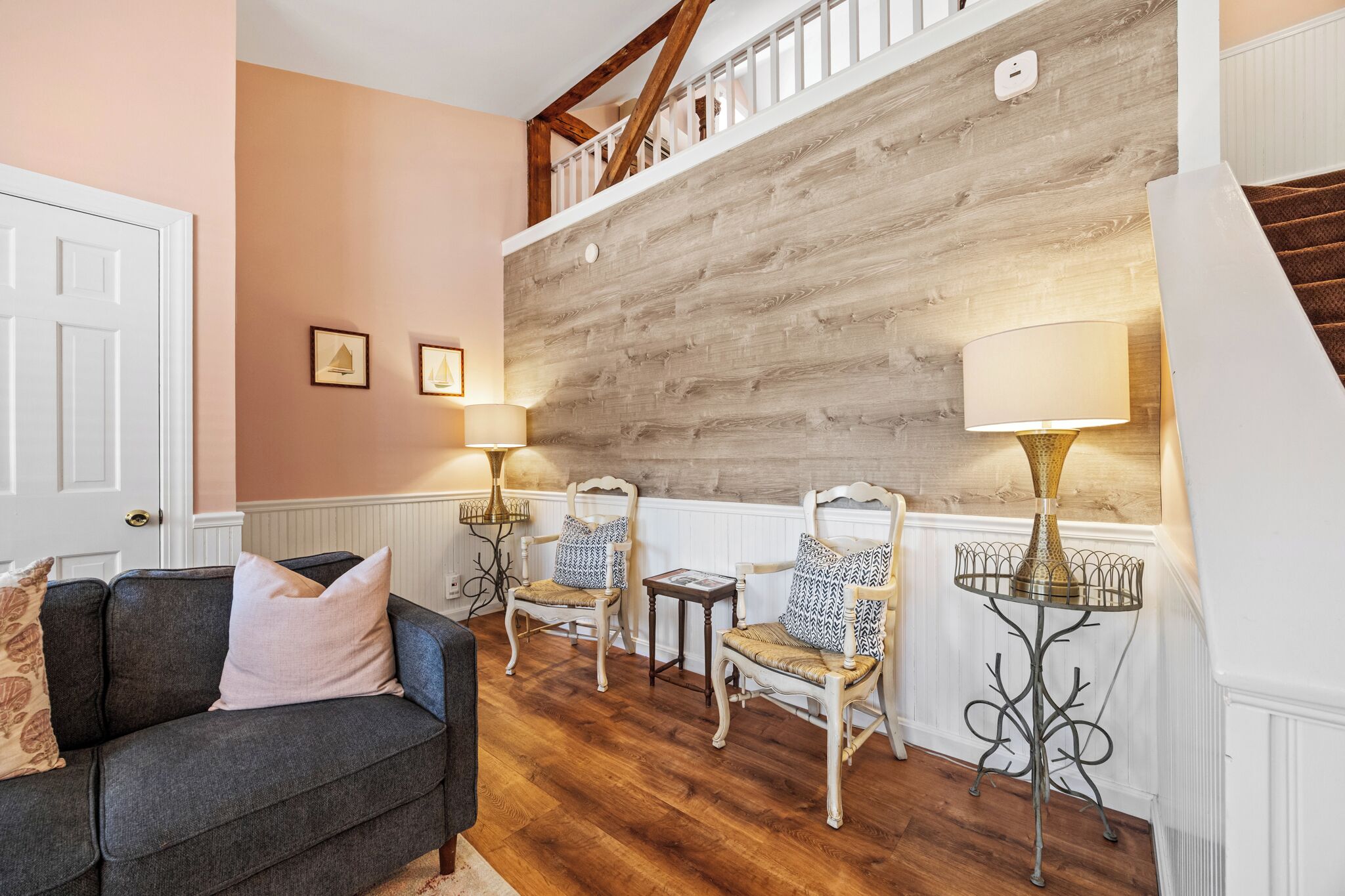 Una sala de estar acogedora con una escalera de madera, un sofá gris, dos sillones y dos lámparas de pie.