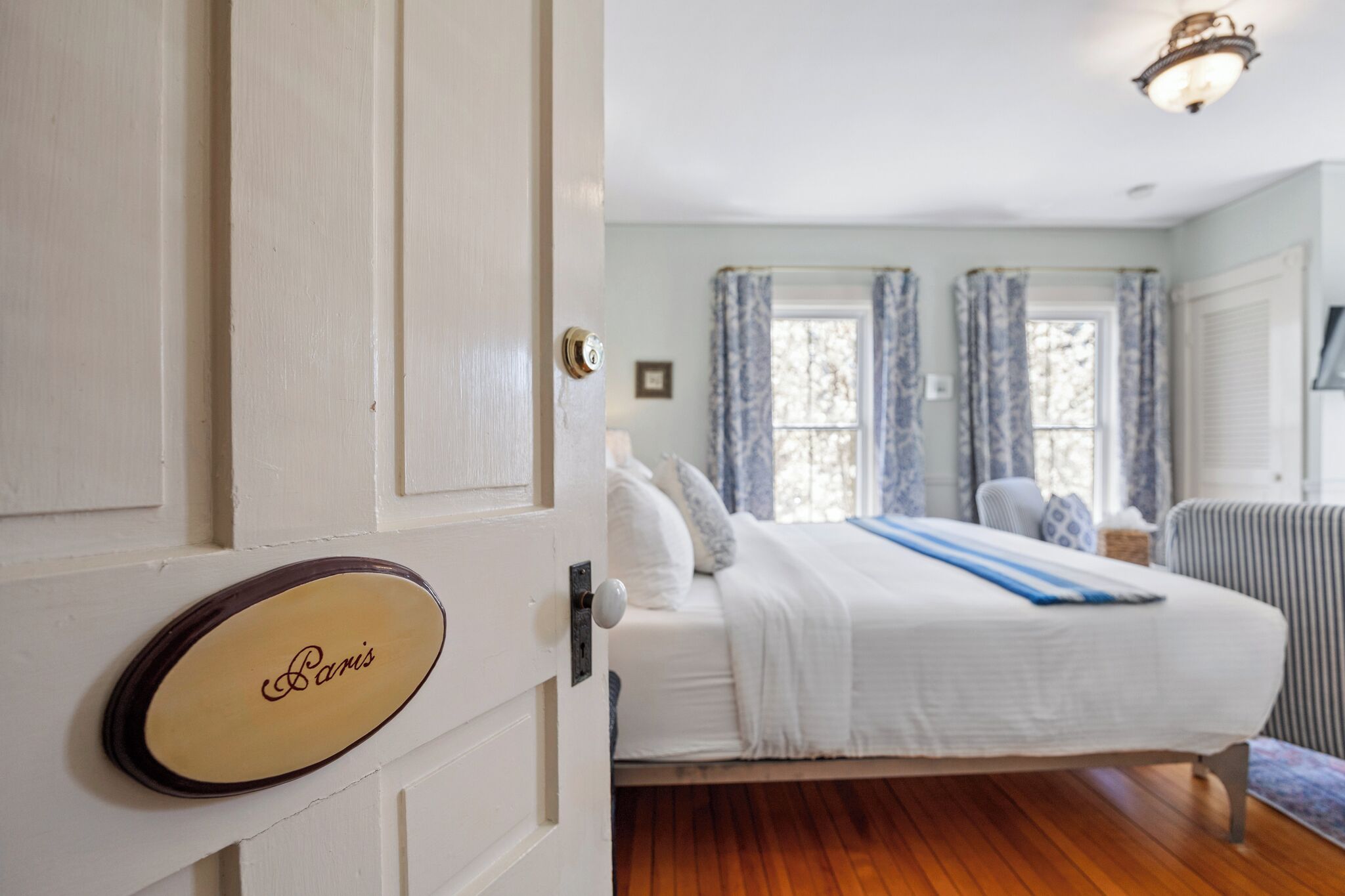 Un dormitorio con una cama, una silla y un ventanal con cortinas.