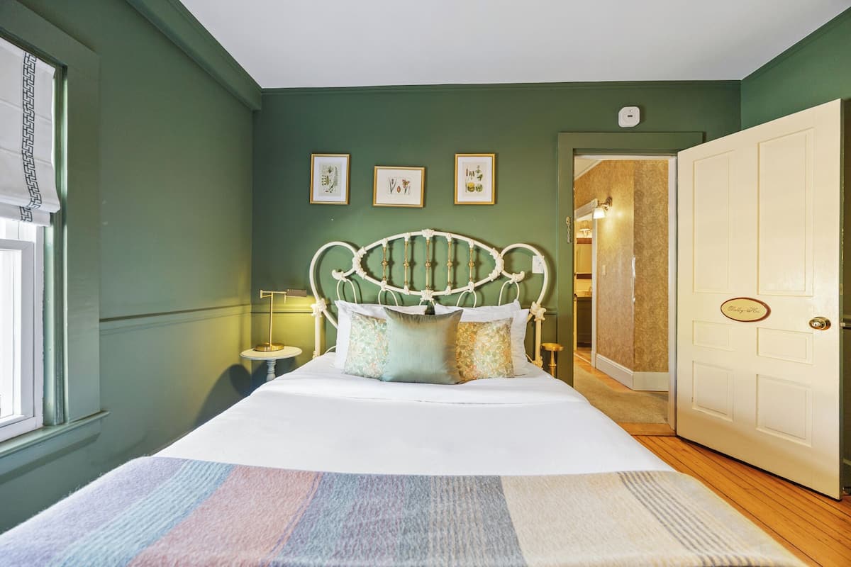 A bedroom with a bed, a nightstand, a door, and framed pictures on the wall.