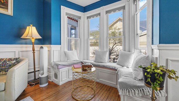 A room with a blue wall, a window seat with a view, a lamp, and a small table with books. - Hartstone Inn (Camden)